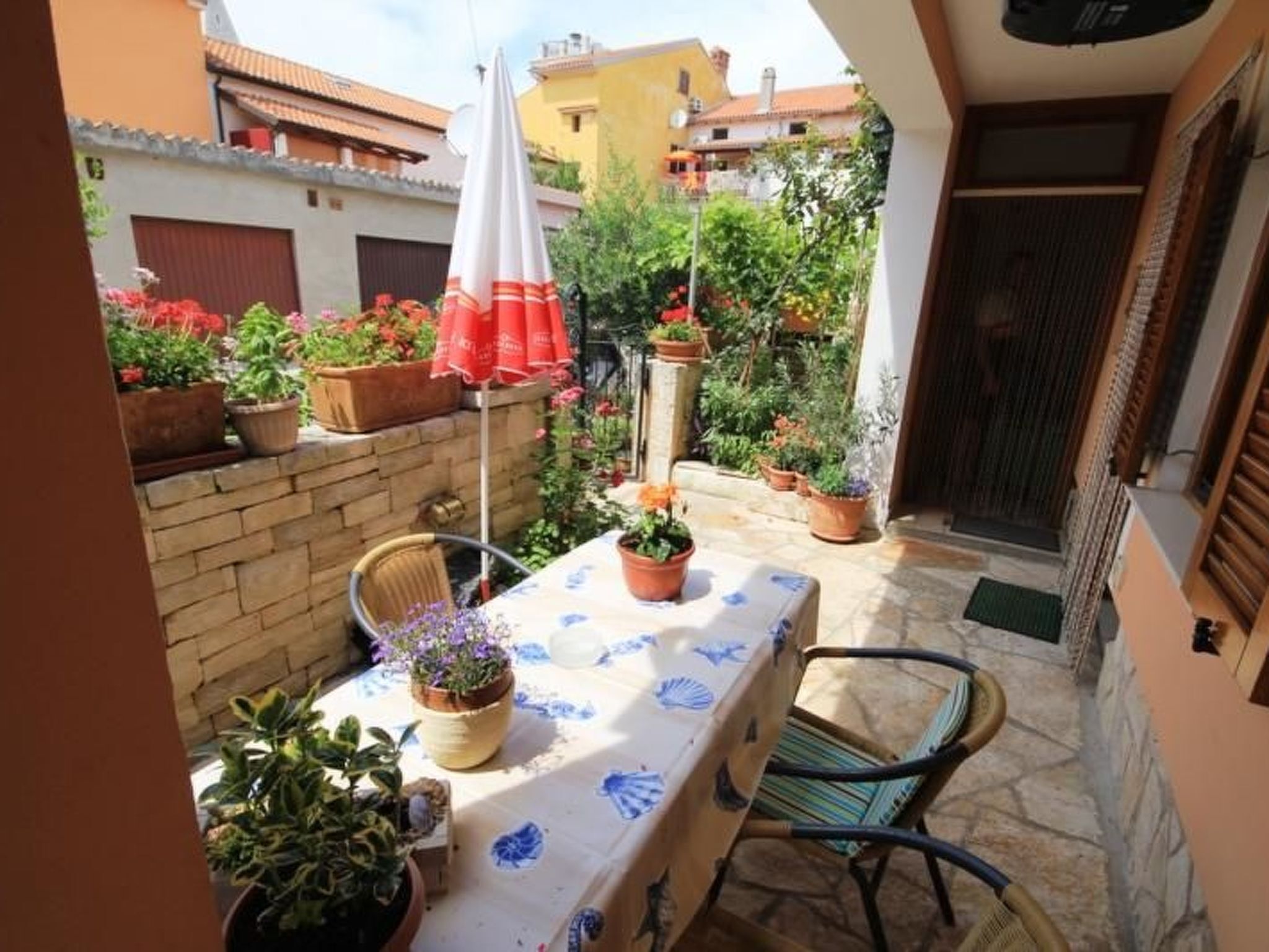 Un patio con una mesa, sillas, plantas en macetas y un paraguas rojo.