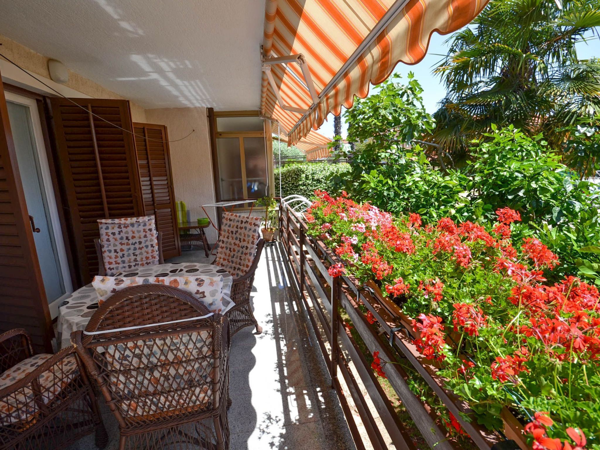 A balcony with wicker furniture, a striped awning, and a railing with red flowers.