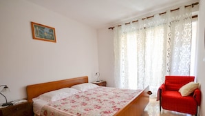 Ein Schlafzimmer mit einem hölzernen Bett, einem Nachttisch, einem roten Sessel und einem Fenster mit gemusterten Vorhängen.