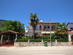 Una casa de dos pisos con un balcón, un muro de piedra y una palmera.