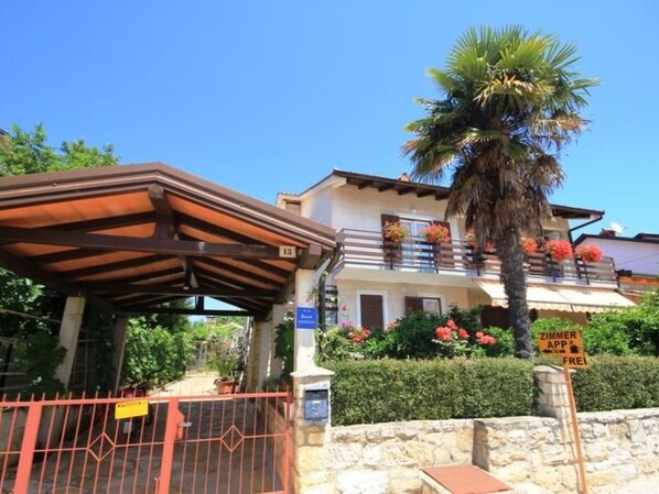 Una casa de dos pisos con un balcón, un patio cubierto y una palmera.