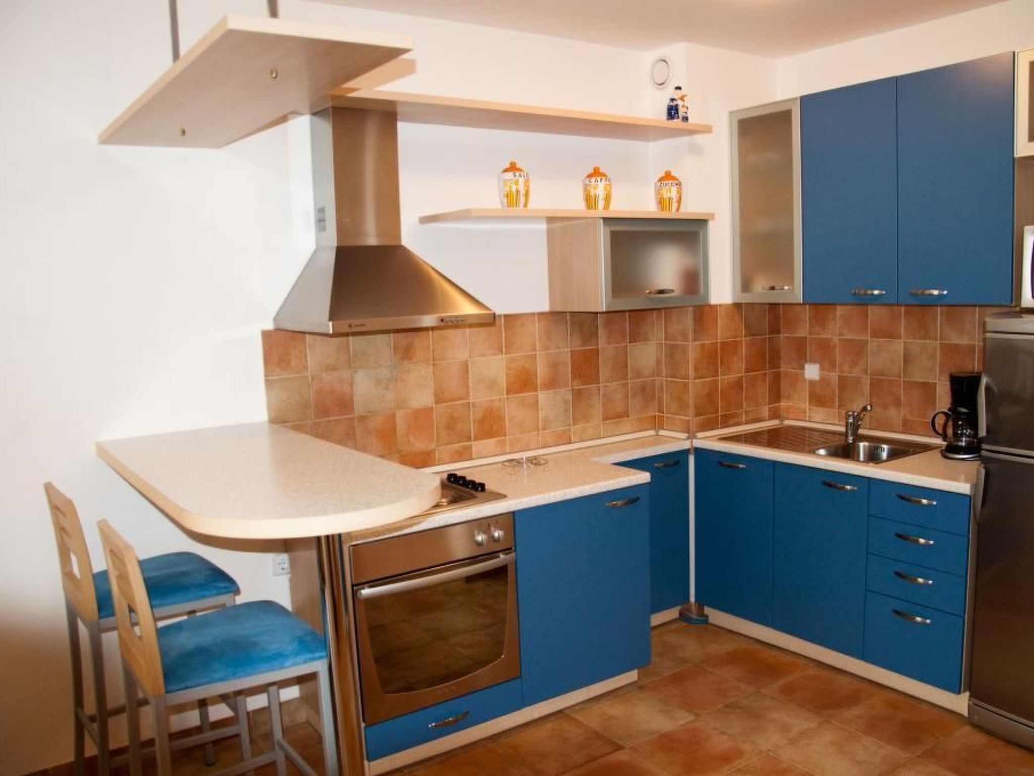 A compact kitchen with blue cabinets, a stainless steel range hood, a built-in oven, and a coffee maker.