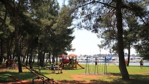 A park with playground equipment, including swings and a slide, surrounded by trees and a body of water in the background. - "Roza" mit Blick auf das Wasser by Interhome (Novigrad (Istra))