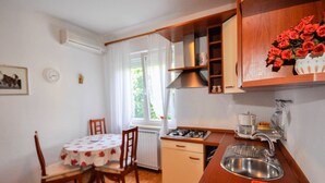 Une cuisine compacte équipée d’une cuisinière à gaz, d’un évier et de meubles en bois. On y trouve une table à manger avec des chaises, ainsi qu’une fenêtre avec des rideaux.