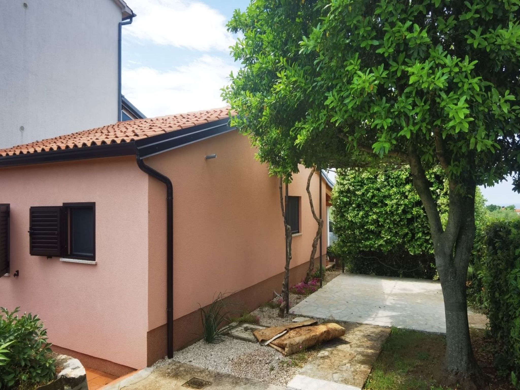 A house with a pink exterior, a tiled roof, and a small garden area with a tree and gravel path.