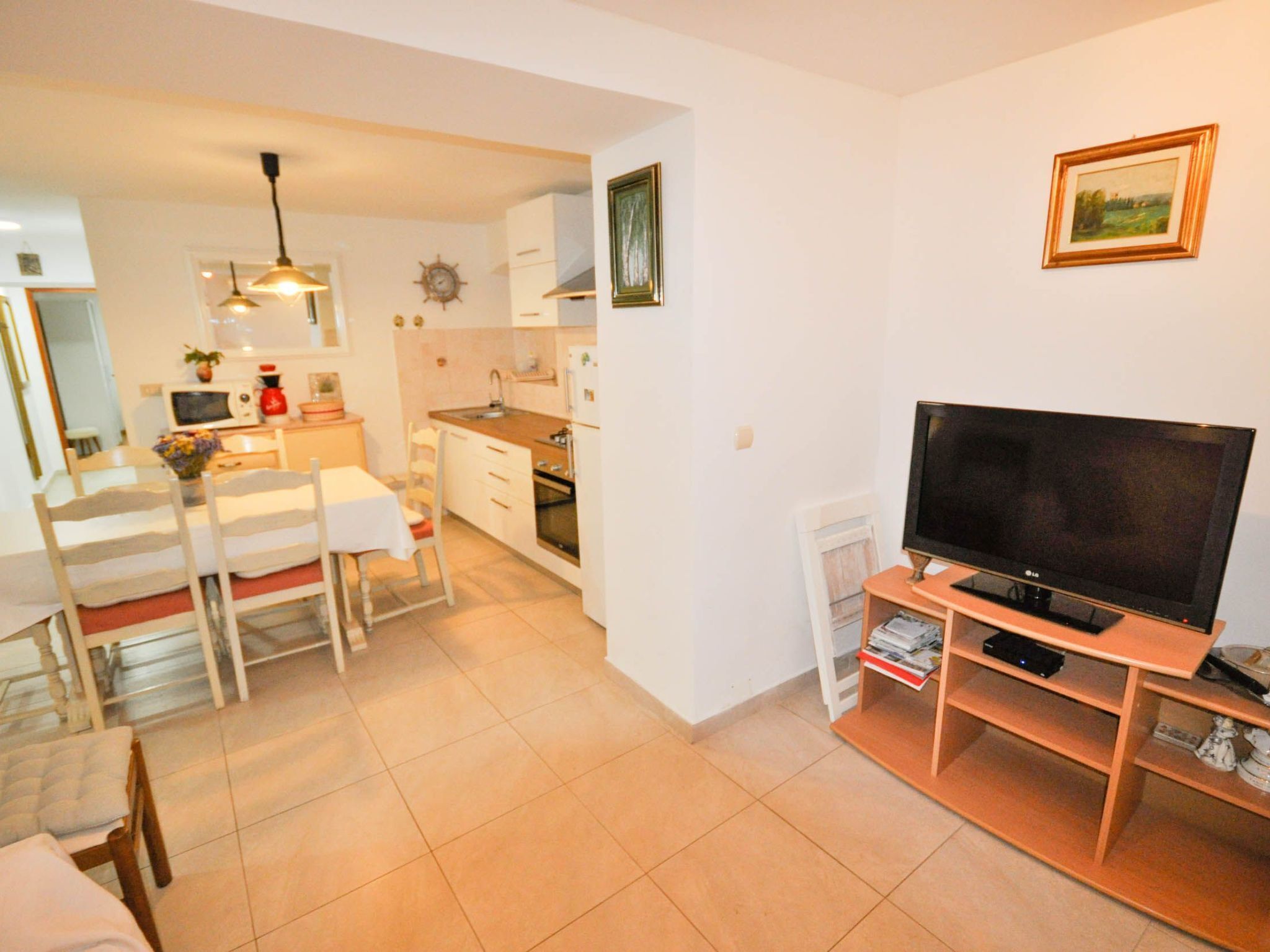 Un espacio habitable compacto con comedor, kitchenette y televisor sobre un atril de madera.