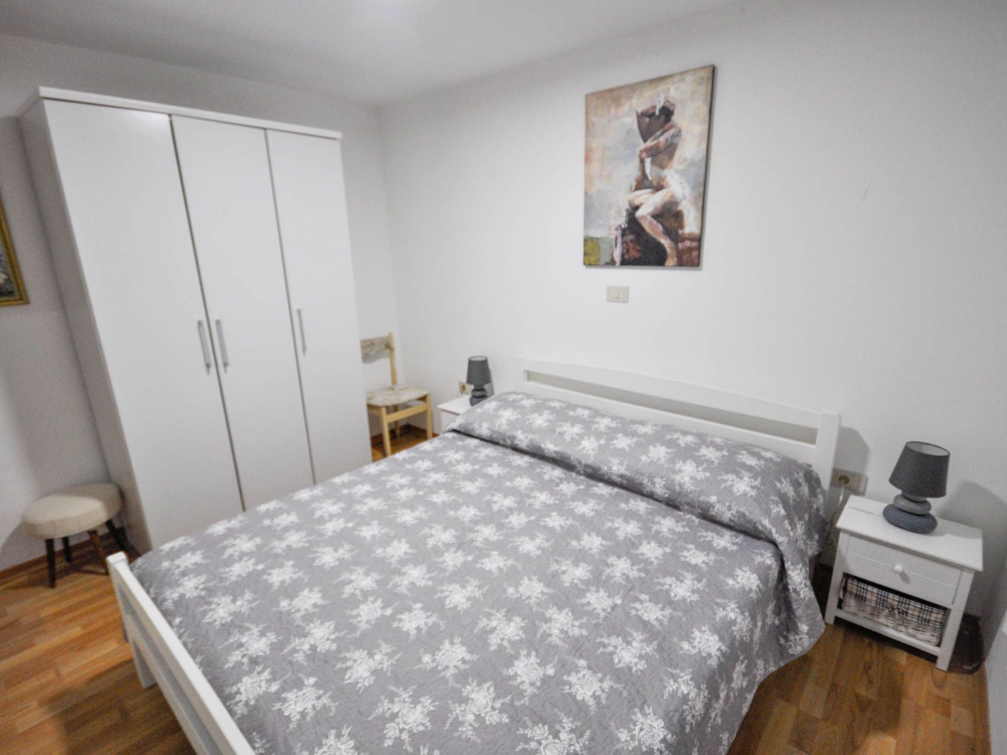 Une chambre à coucher avec un lit, une table de chevet, une chaise, une armoire et un tableau au mur.