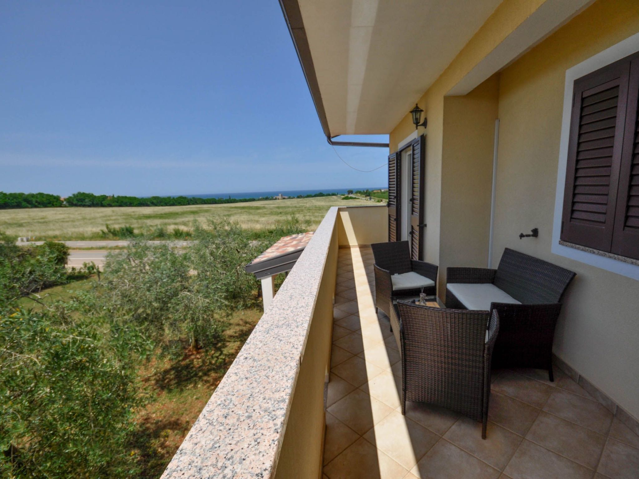 A balcony with outdoor furniture, a view of the countryside, and a clear sky.