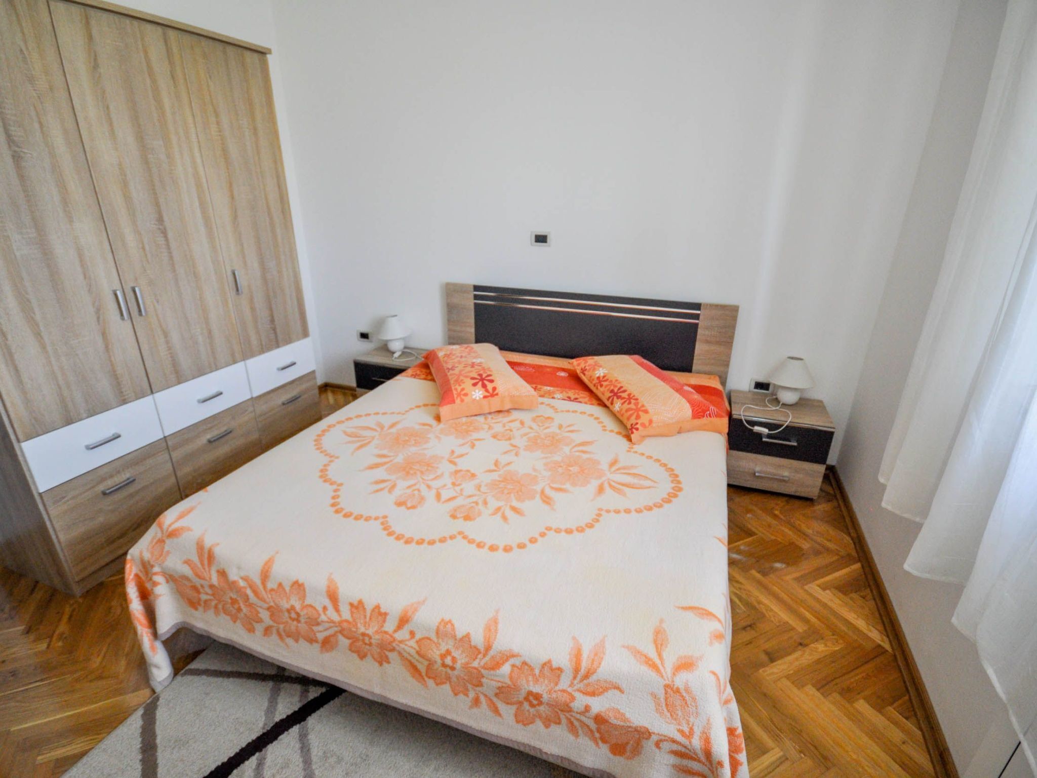 A bedroom with a bed, a wardrobe, a nightstand, and a lamp.