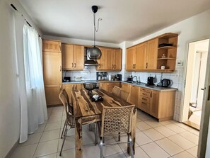 A modern kitchen with wooden cabinets, a dining table with chairs, and a hanging light fixture. - Haus Marija**** by Interhome (Umag/Juricani)