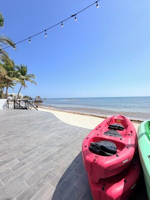 A beachside walkway with kayaks, palm trees, and a clear blue sky.