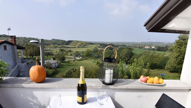 En balkon med et bord dækket til to personer, der viser en champagneflaske, en granatæble og en tallerken med appelsiner.