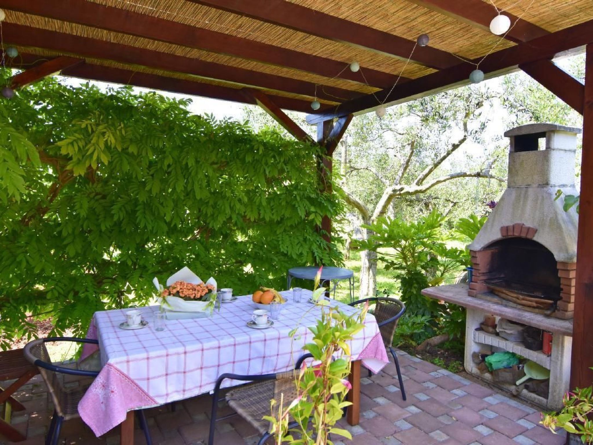 An outdoor patio with a table set for dining, a brick oven, and lush greenery.