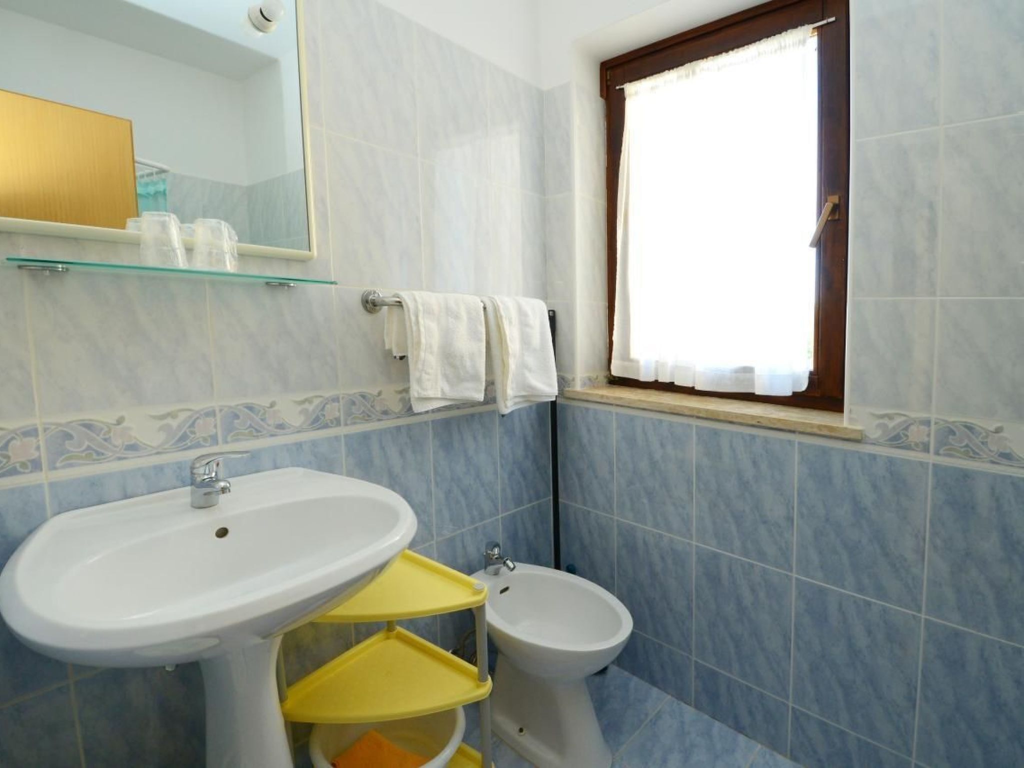 Un baño con lavamanos, bidé y ventana con cortinas.