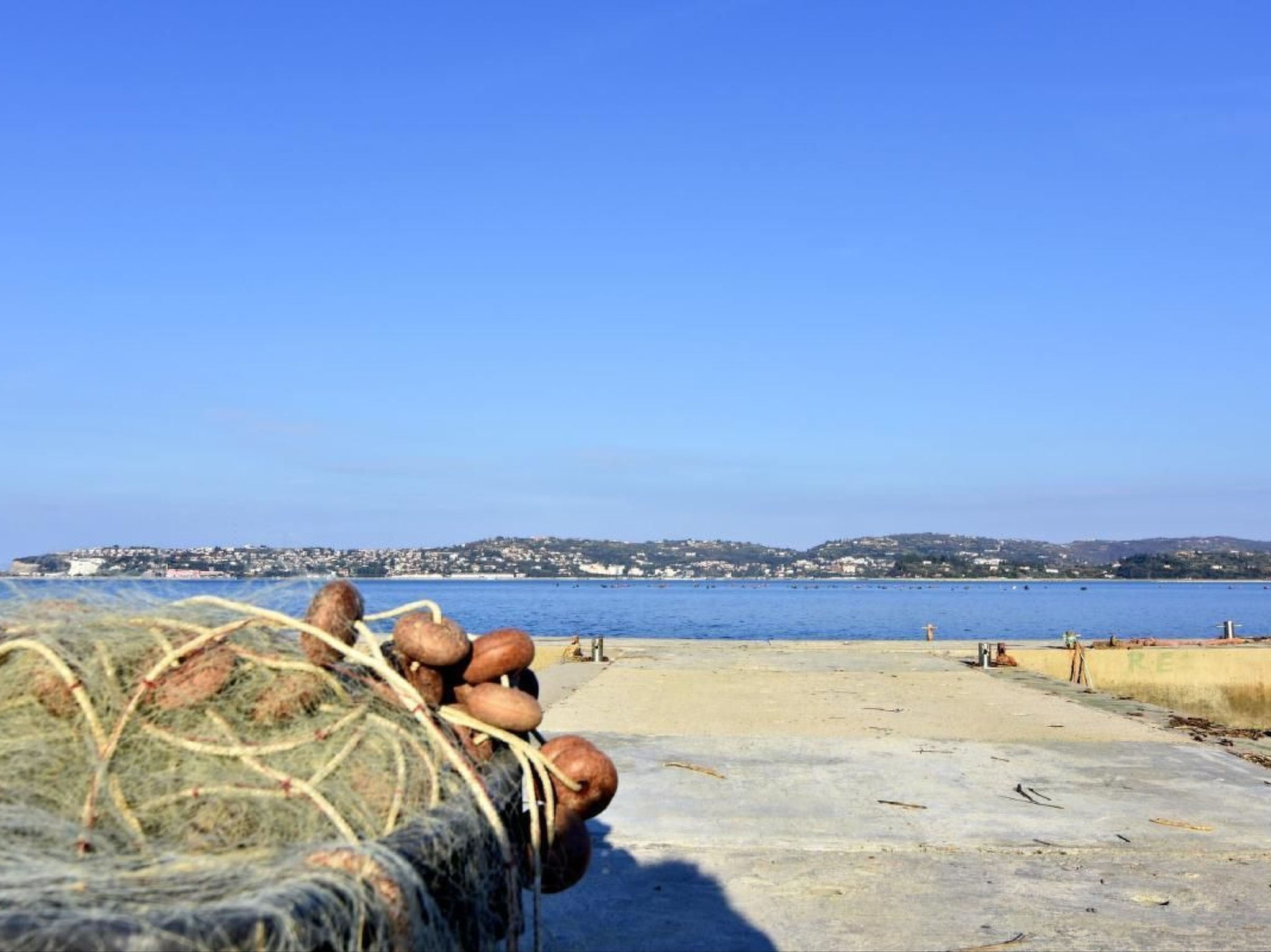 A beach with a clear blue sky, a sandy area, and a distant view of a town across the water.