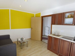 A compact kitchen with wooden cabinets, a glass table, and a yellow accent wall. - Wohnung in Zambratija mit Schöner Terrasse by Interhome (Umag/Zambratija)