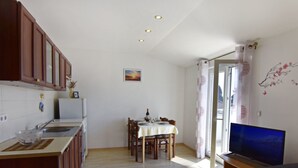 A compact kitchen with wooden cabinets, a dining area with a table and chairs, a television, and a window with curtains. - Wohnung in Zambratija mit Schöner Terrasse by Interhome (Umag/Zambratija)