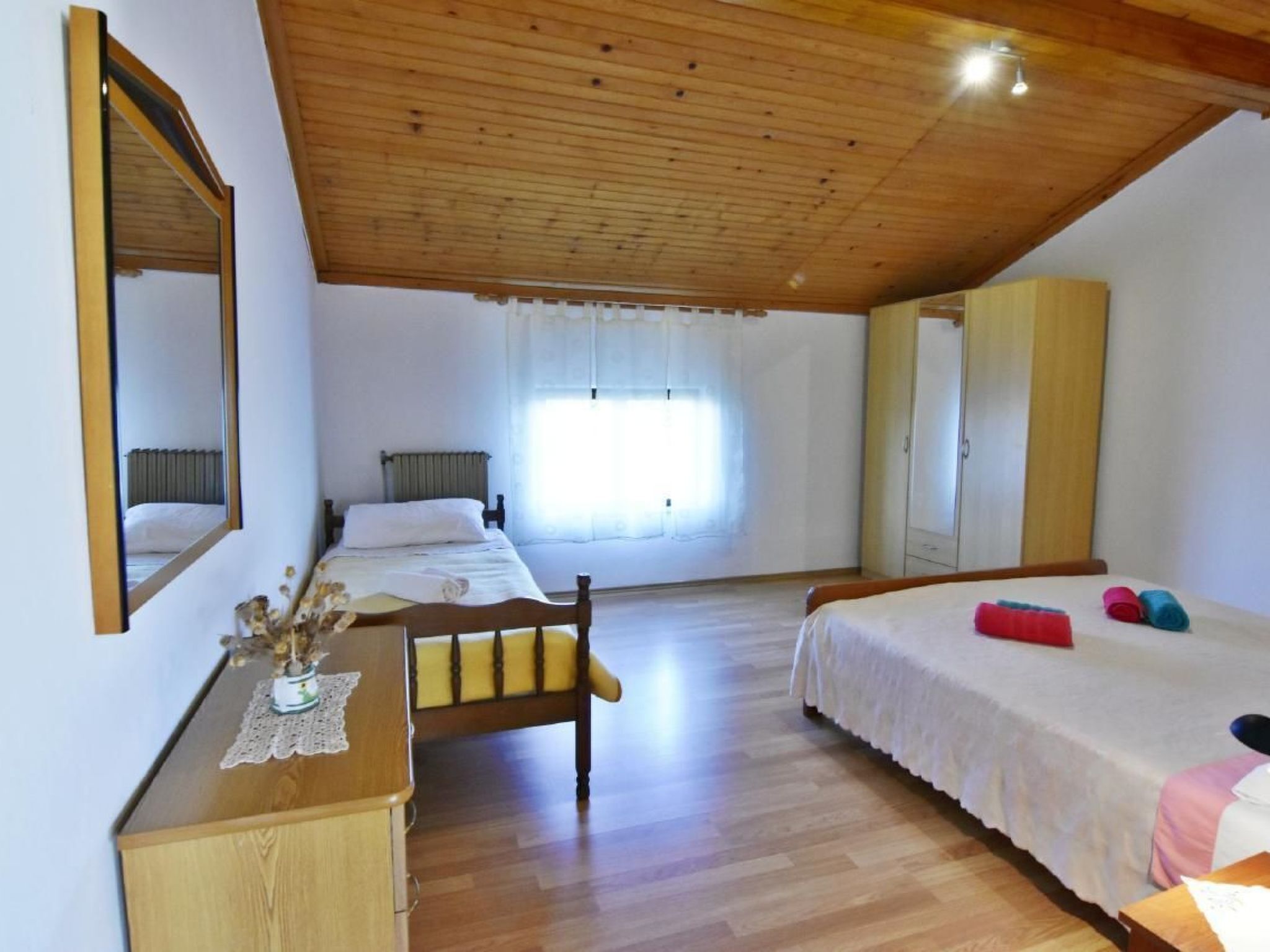 A bedroom with two beds, a wooden desk, a chair, a wardrobe, and a large mirror.