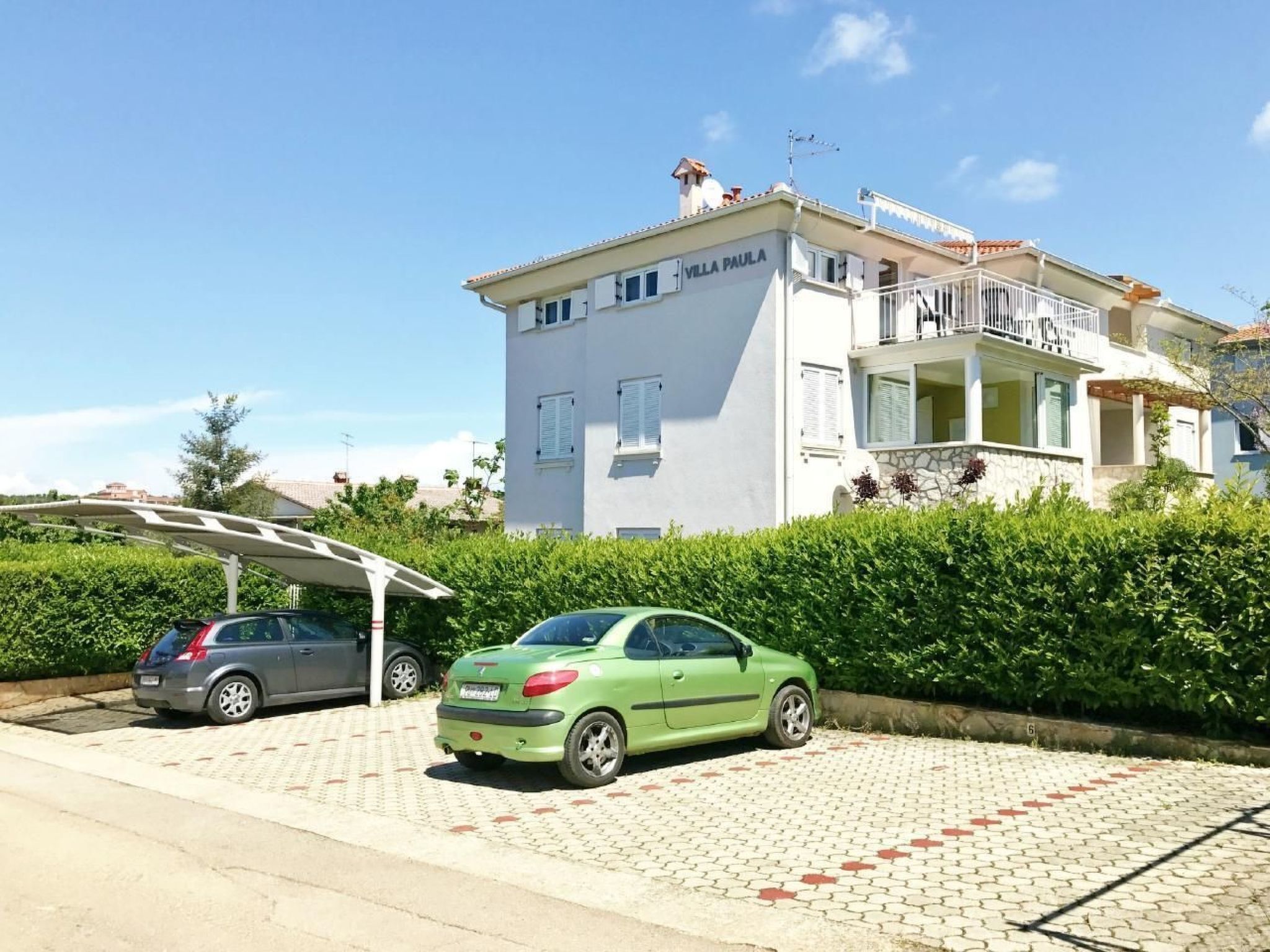 Une villa à deux étages, nommée « Villa Paula », avec une allée pavée et des voitures garées.