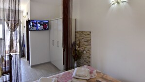 Ett hotellrum med en säng, en tv på väggen, en dusch och en väggpanel i trä.