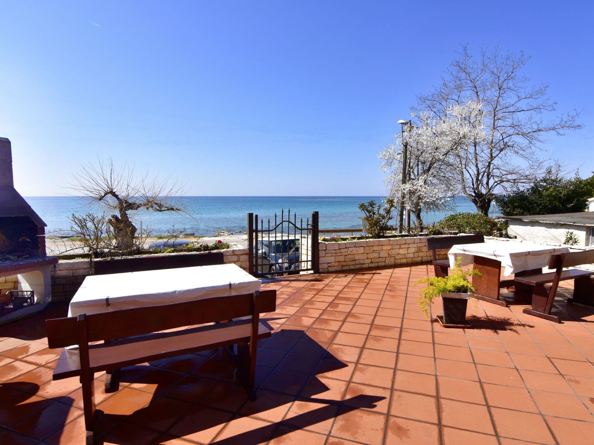An outdoor patio with a view of the sea, a barbecue grill, and a table with a white tablecloth.
