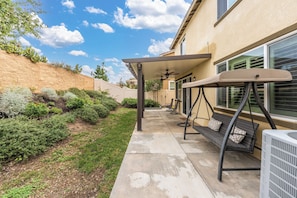 A patio with a swing chair, a ceiling fan, and a covered seating area. - Riverside Insurance Housing/ Furnished 4BR/3BA/ Pets Welcome/ 31+ nights (Riverside)