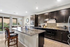 A modern kitchen with dark cabinetry, a granite countertop, and a large island with bar stools. - Riverside Insurance Housing/ Furnished 4BR/3BA/ Pets Welcome/ 31+ nights (Riverside)