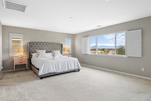 A bedroom with a large bed, two bedside tables with lamps, a window with shutters, and a view of the outdoors. - Riverside Insurance Housing/ Furnished 4BR/3BA/ Pets Welcome/ 31+ nights (Riverside)