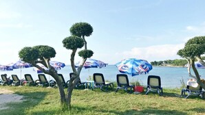 Un espace aménagé au bord de la plage, avec des rangées de chaises et de parasols, une vue dégagée sur la mer et des arbres soigneusement taillés.