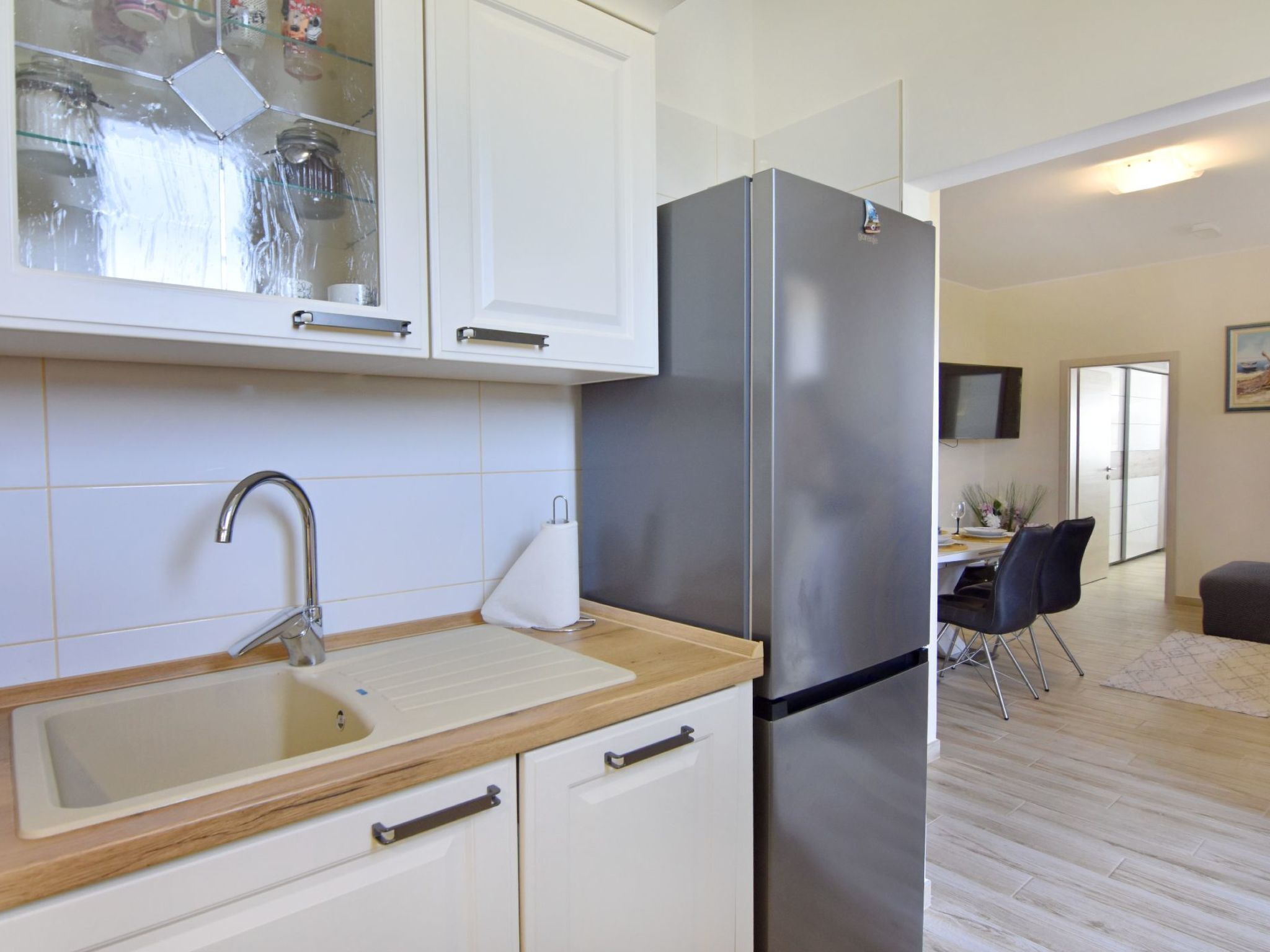 A modern kitchen with a stainless steel refrigerator, white cabinets, a wooden countertop, and a sink.