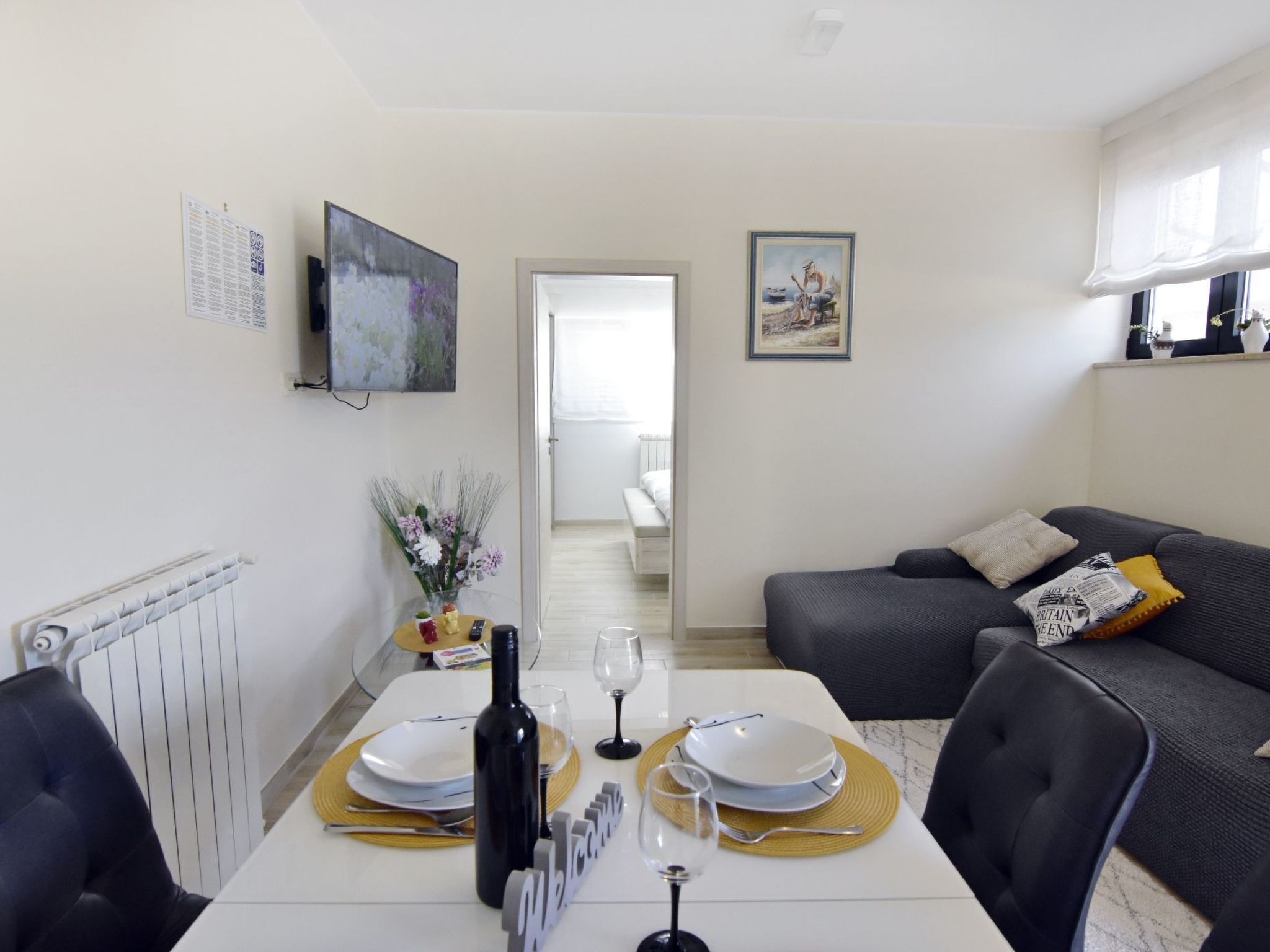 Een eethoek met een tafel gedekt voor twee personen, een bank en een televisie aan de muur.