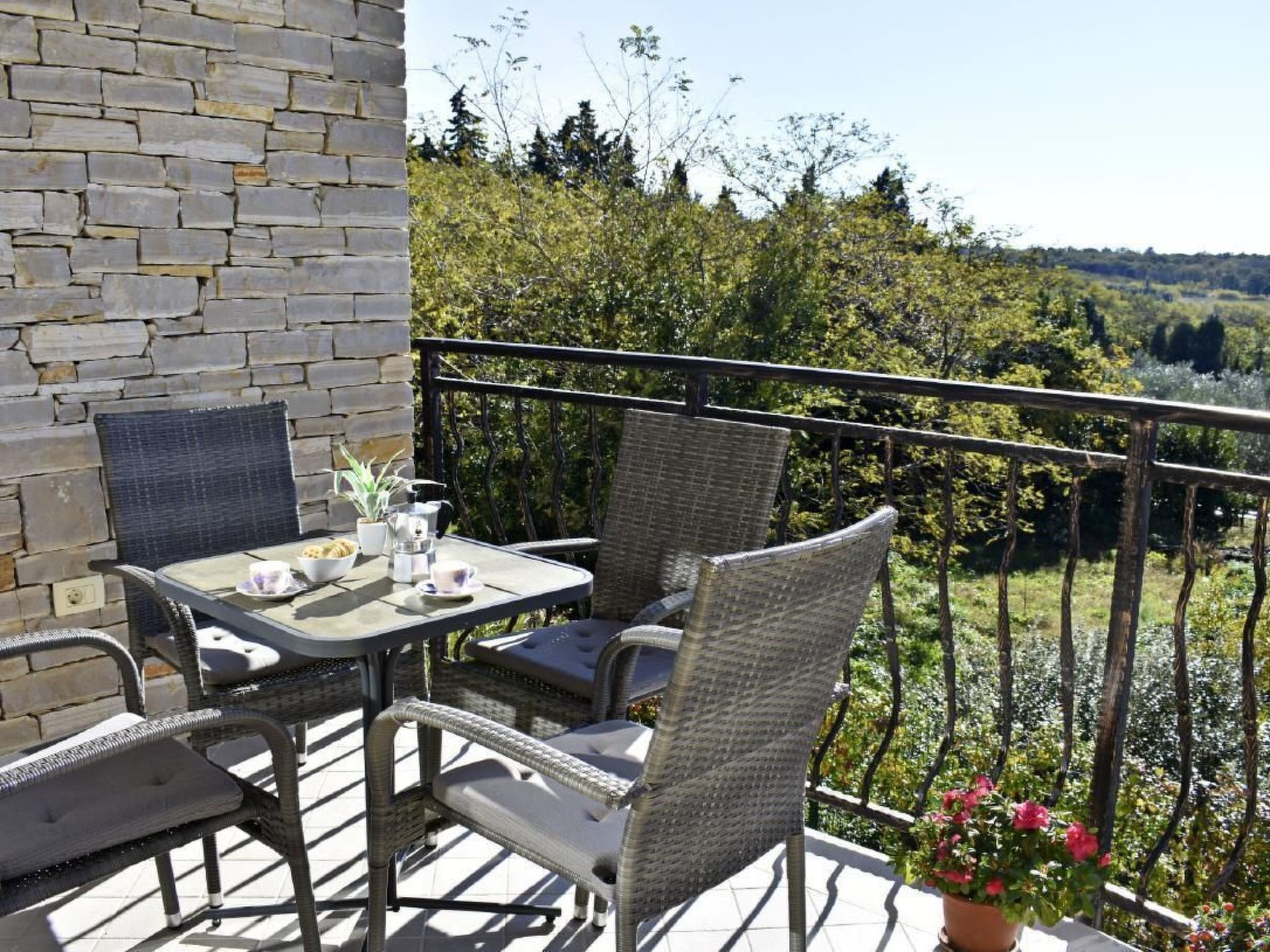 A balcony with wicker furniture and a table set for two, overlooking a lush landscape.