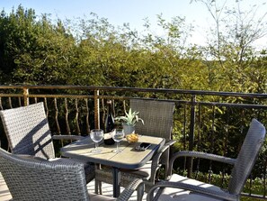 Un balcon agrémenté de meubles en osier, une table, deux verres à vin, une bouteille, une plante et un bol de collations.