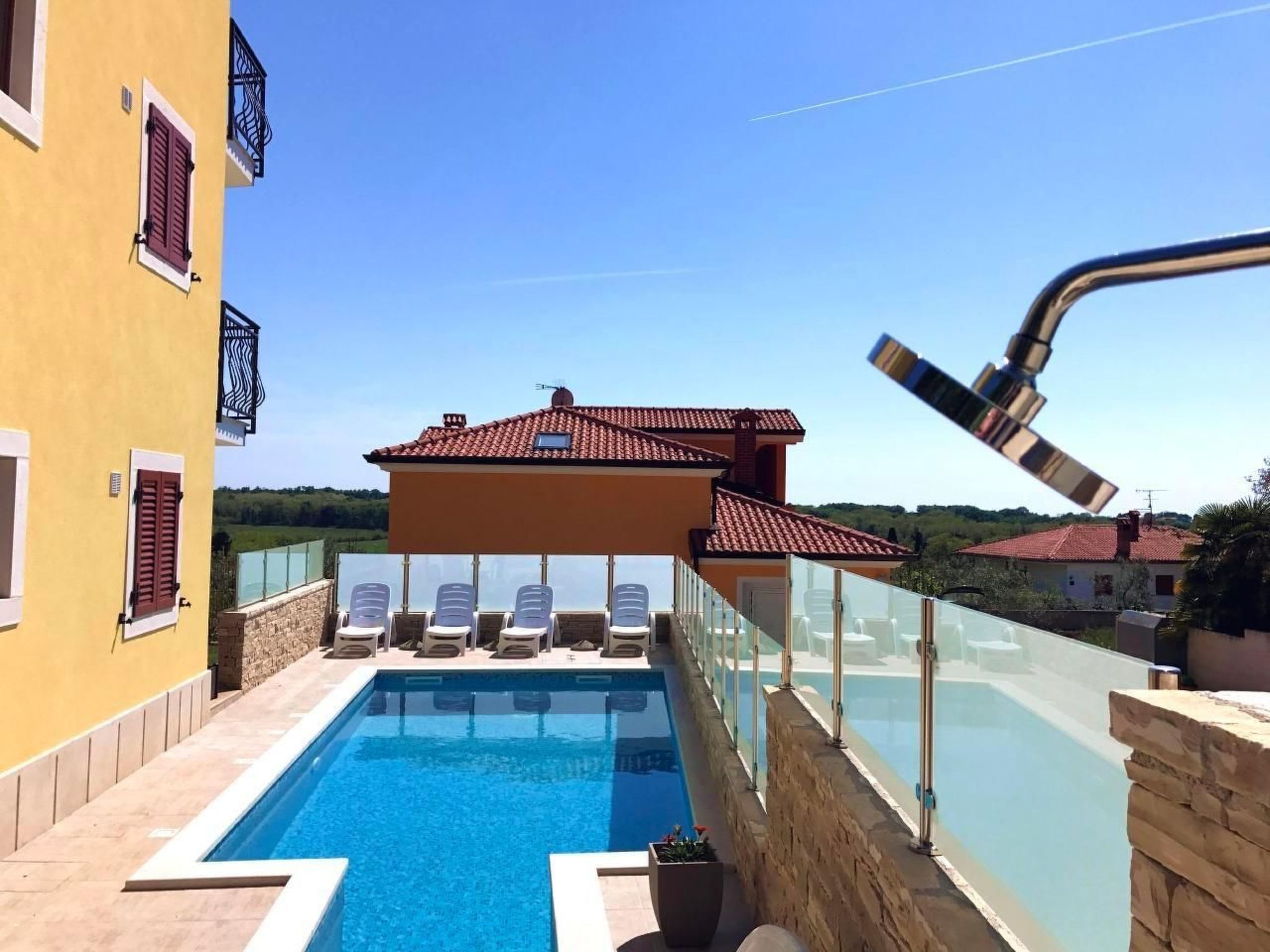 Zona de piscina con sillones, cielo despejado y un edificio con techo de tejas rojas.