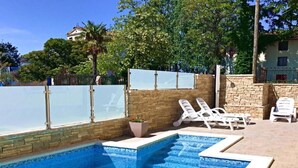 Une piscine à l’eau d’un bleu cristallin, entourée de chaises longues blanches et d’un mur en pierre.
