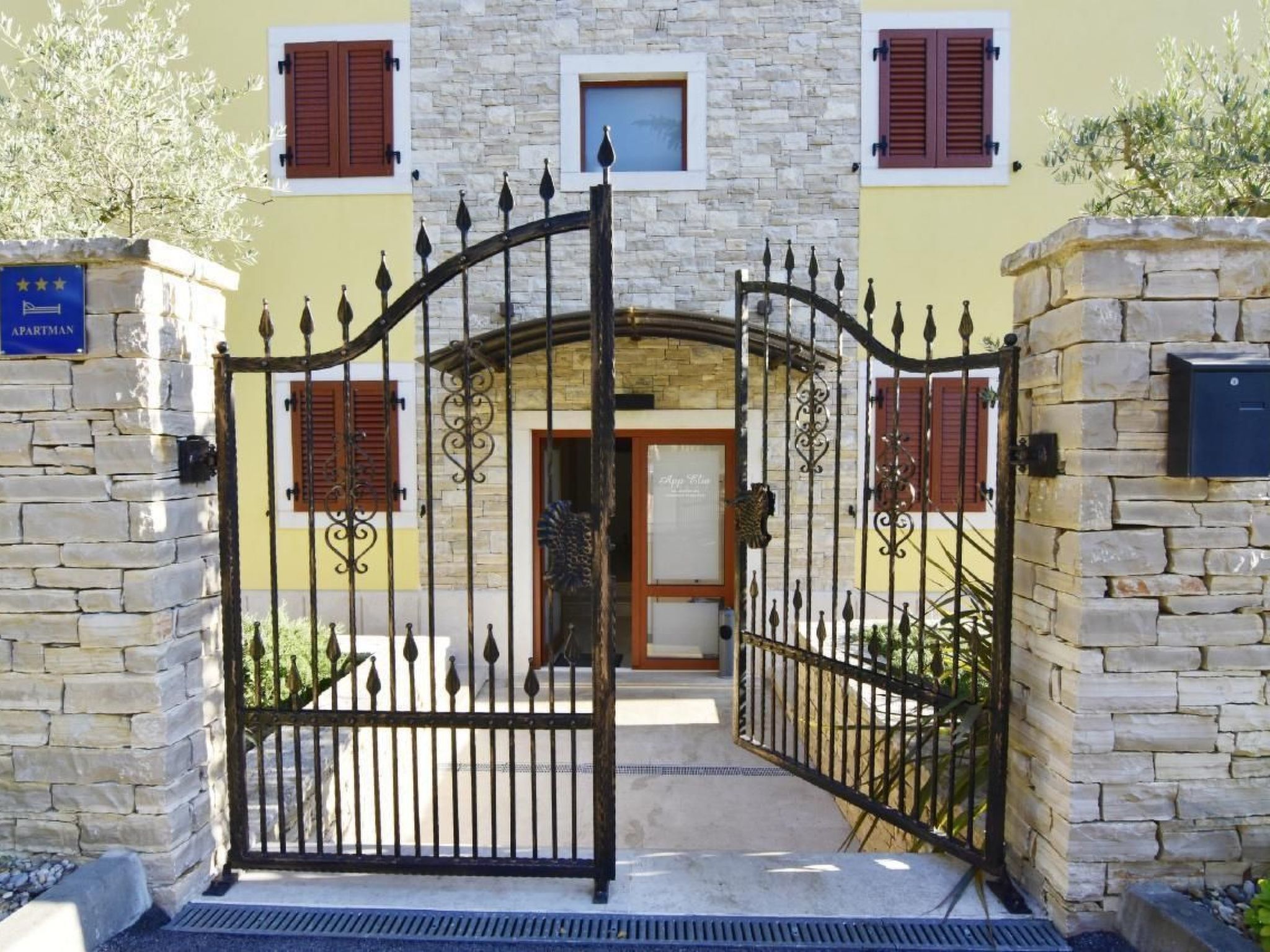 A stone-walled building with a gated entrance, a mailbox, and a sign indicating it is an apartment.