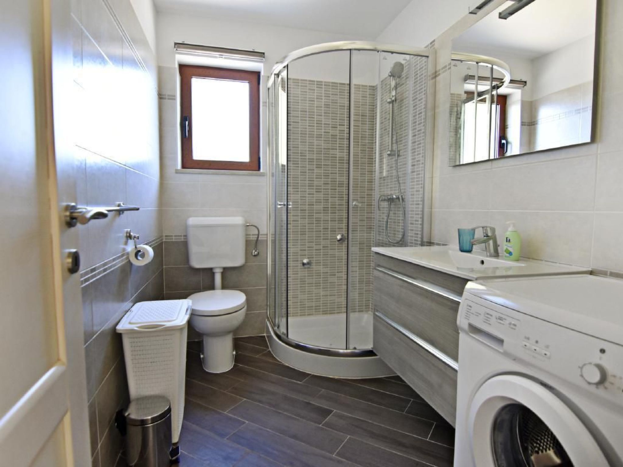 A compact bathroom with a toilet, shower, and washing machine.