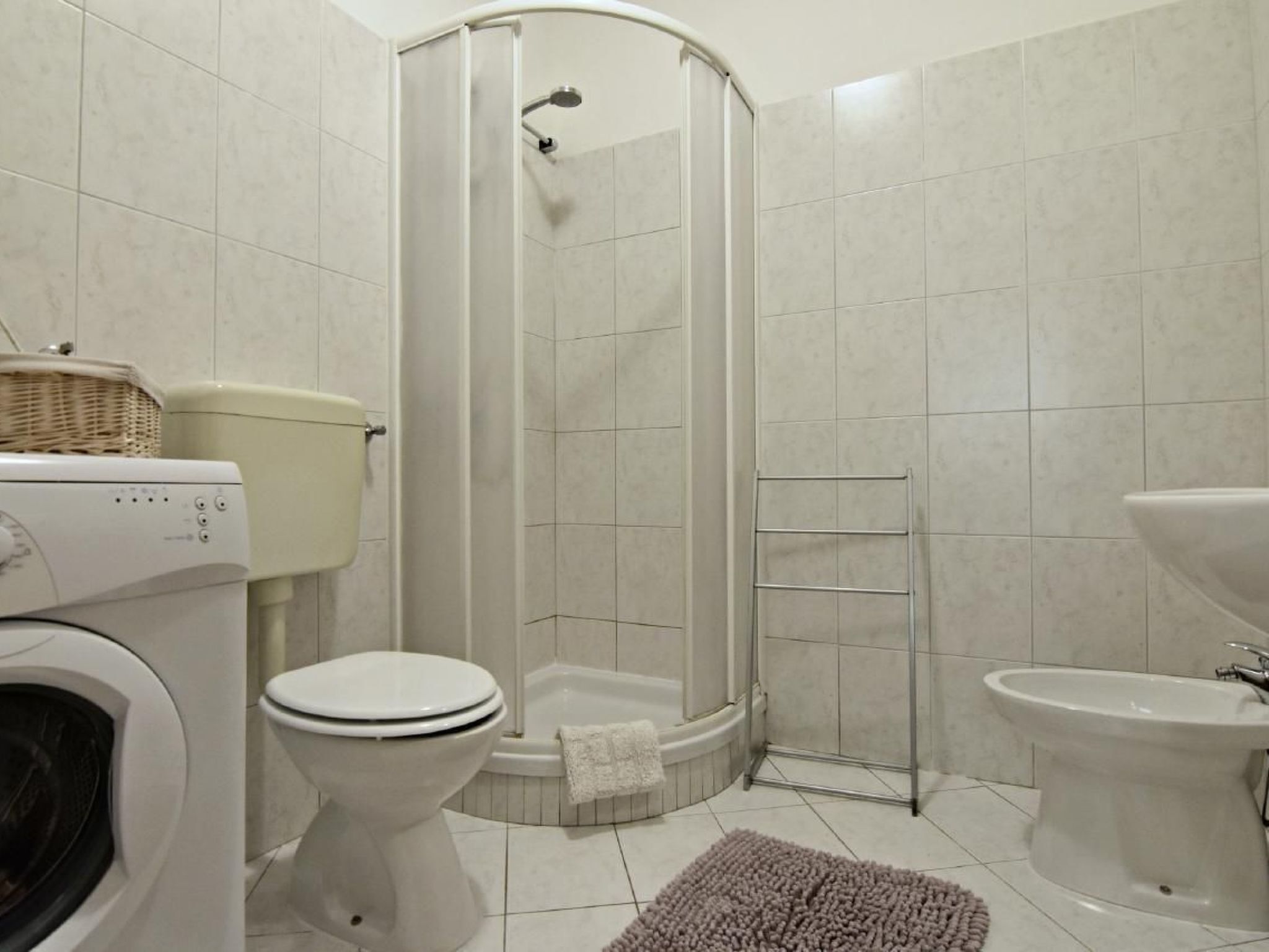 A bathroom with a toilet, washing machine, bidet, and a shower stall.