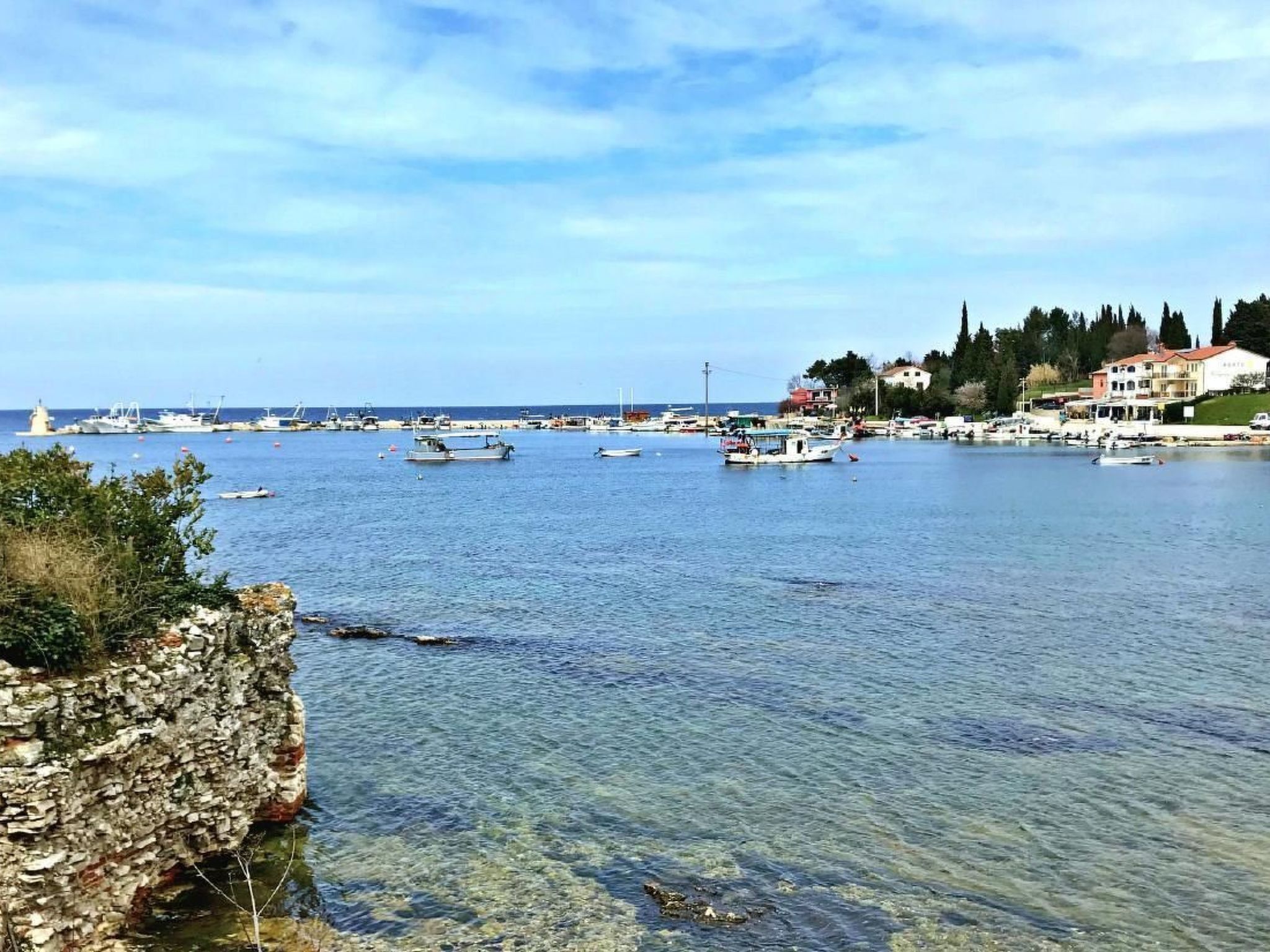 A coastal marina with boats, clear water, and buildings in the background.