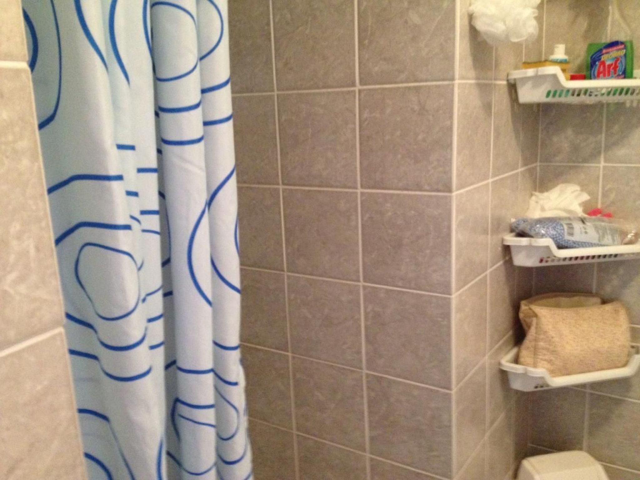 A bathroom with a shower curtain, tiled walls, and shelves holding toiletries.