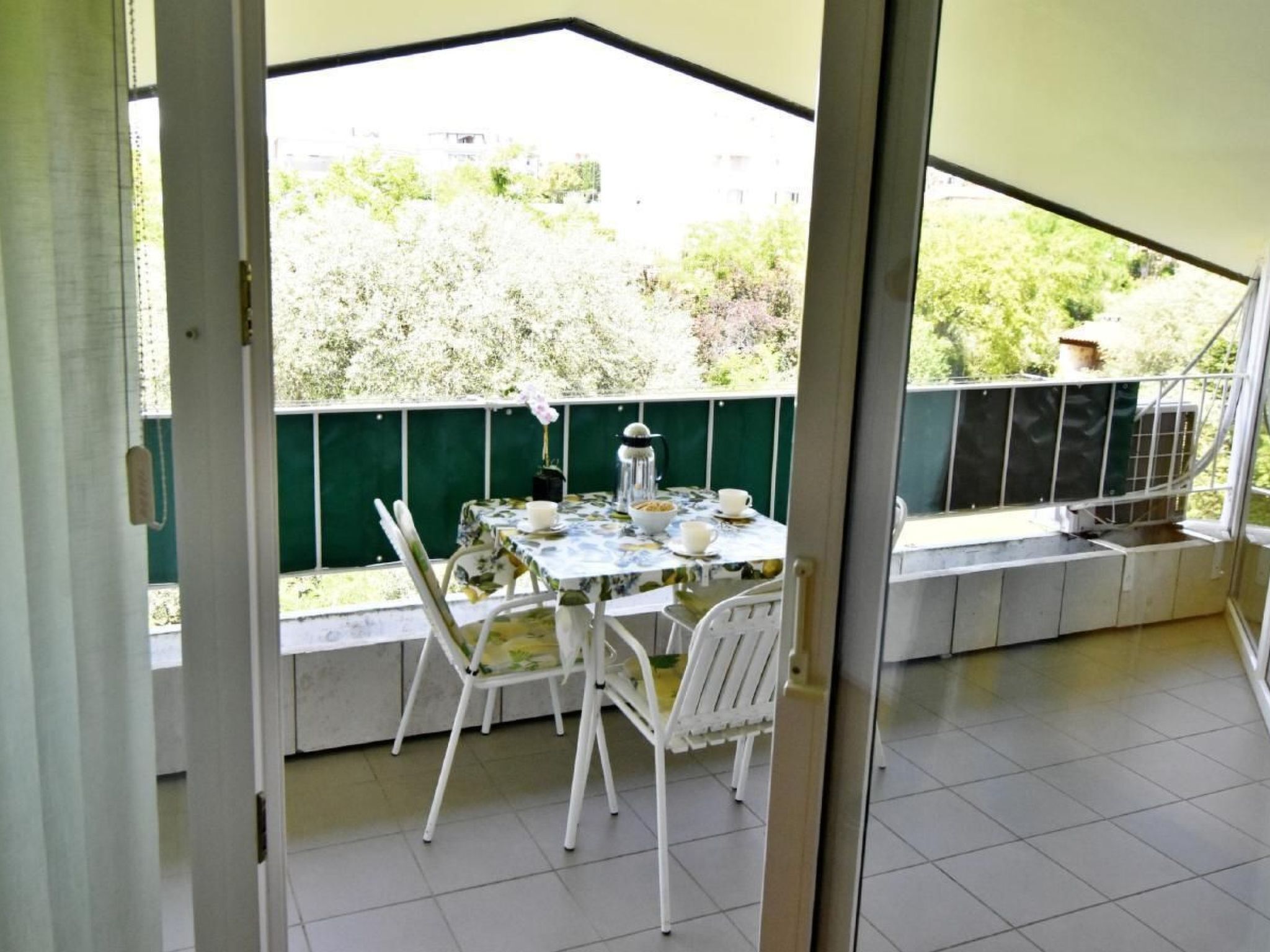 A patio area with a table and chairs, a small table with a flower vase, and a view of greenery outside.