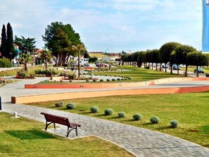A park with a paved walkway, a bench, and neatly trimmed grass. - APP EVA by Interhome (Umag/Savudrija)