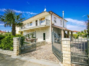 Une maison à deux étages avec une façade en pierre, un balcon et une entrée fermée par un portail.
