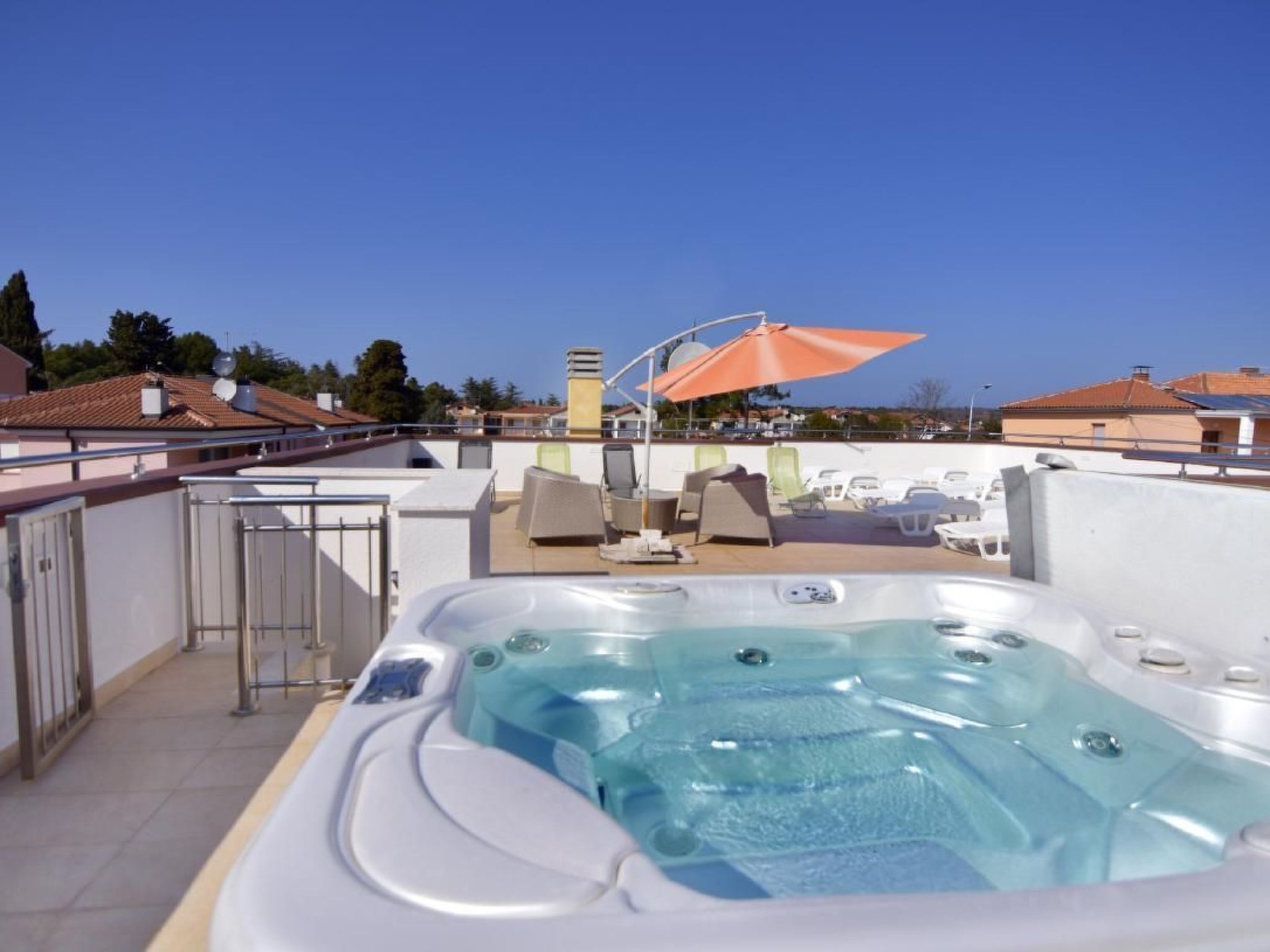 A rooftop pool area with a hot tub, lounge chairs, and an umbrella.