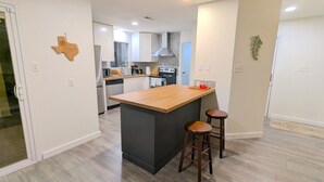 Una cocina moderna con una isla central, taburetes de bar y un microondas.