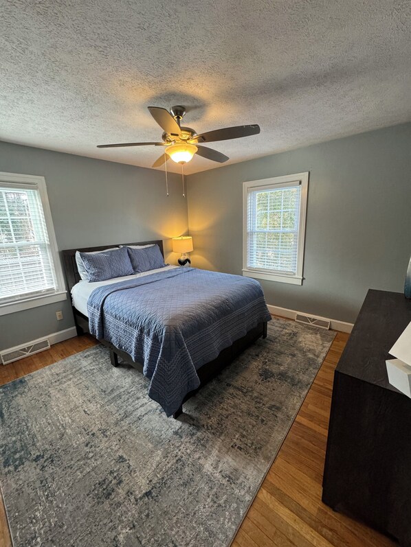 A bedroom with a bed, a ceiling fan, a nightstand, and a window with blinds. - Perfect 4BR Getaway in Prime Location (Russellville)