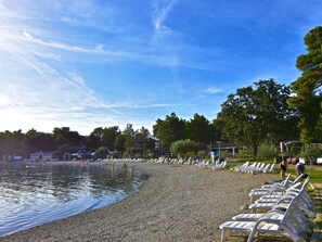 A pebbled beach with lounge chairs and a calm water body. - LINO B4 by Interhome (Umag)
