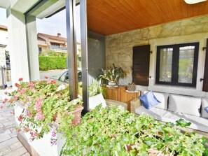 Un espacio de estar al aire libre cubierto, con pared de piedra, plantas en macetas y vista a la calle.