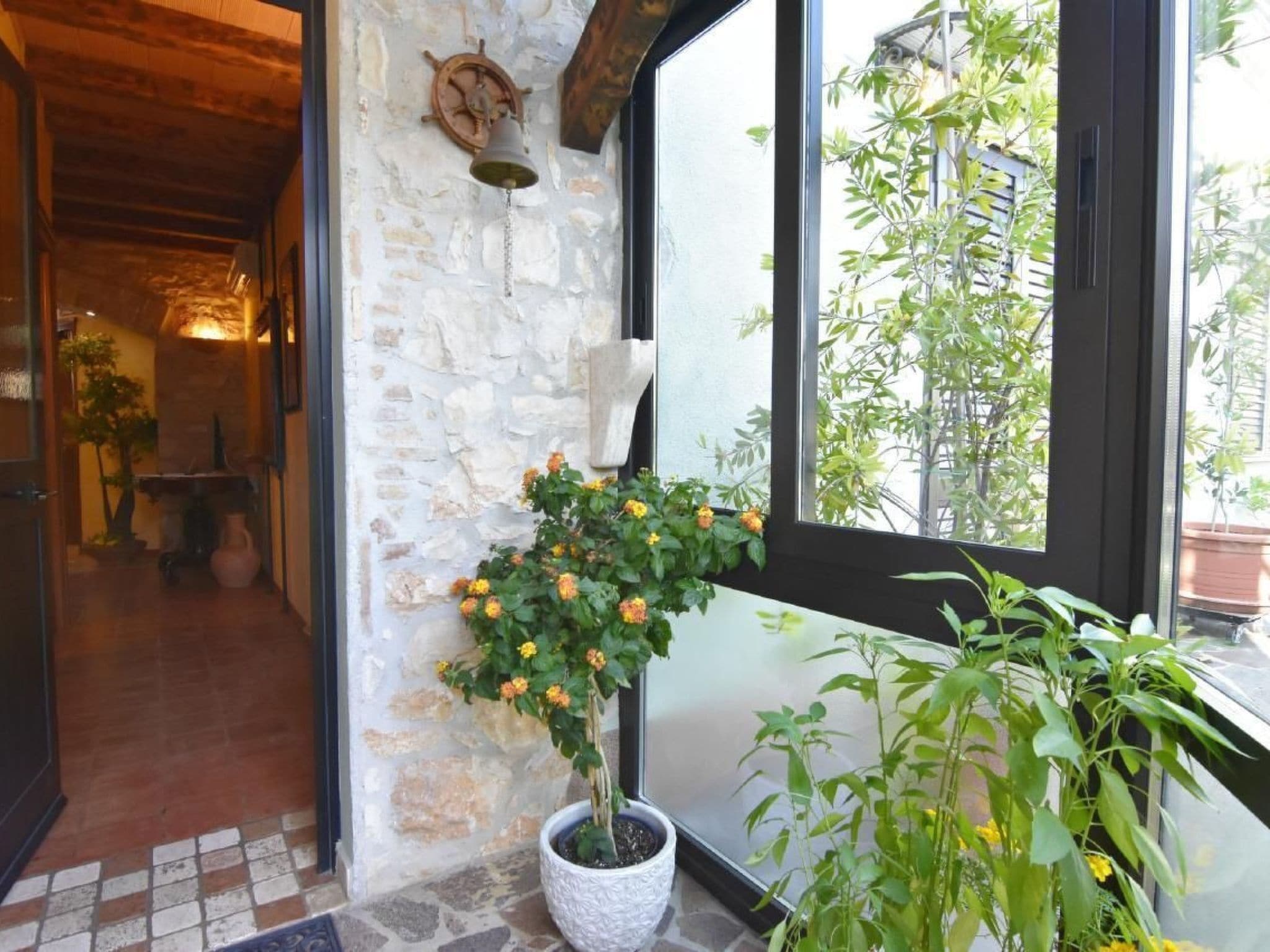 A stone wall with a potted plant and a bell.