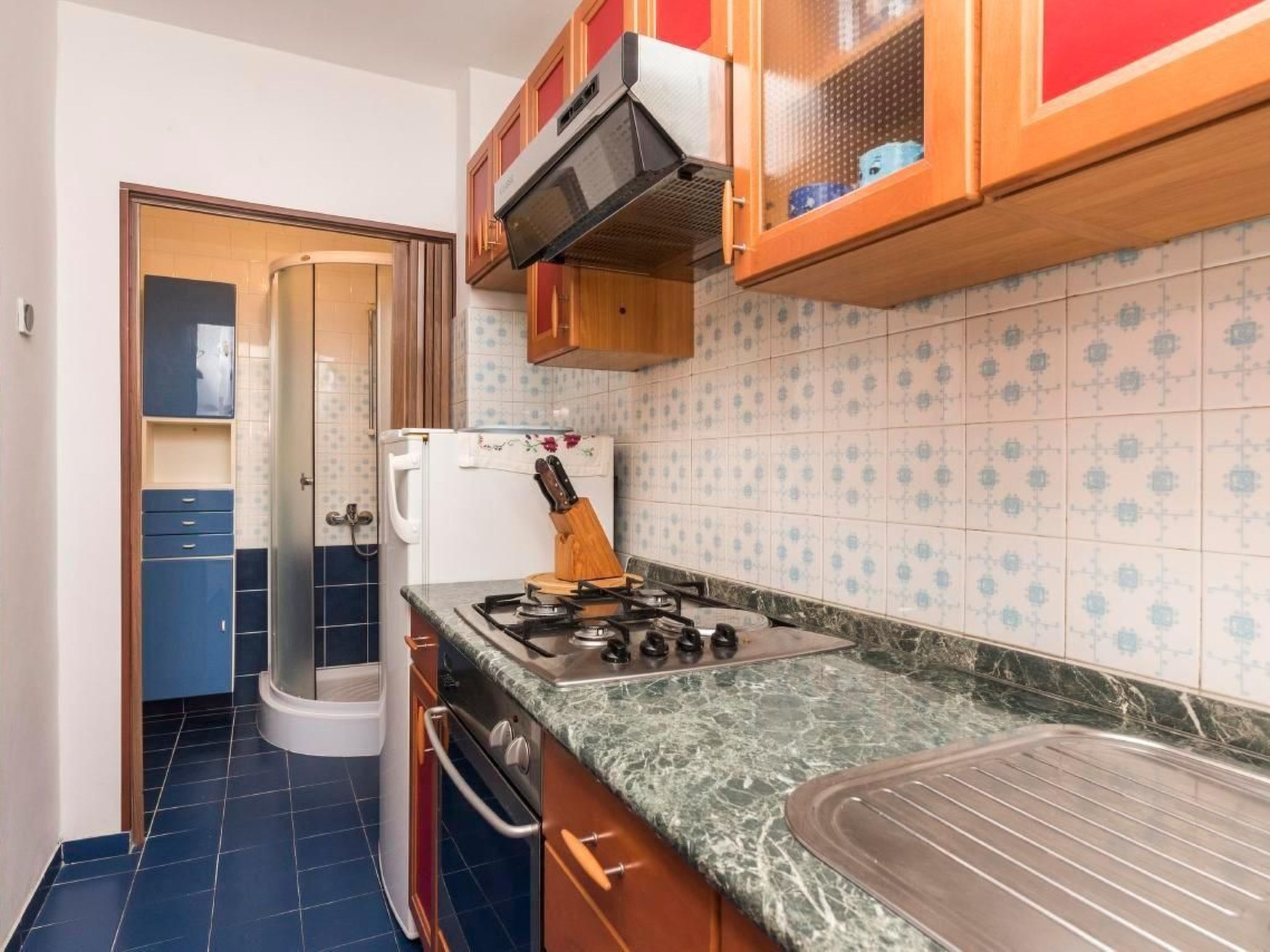 A compact kitchen with a gas stove, a refrigerator, and blue cabinets.